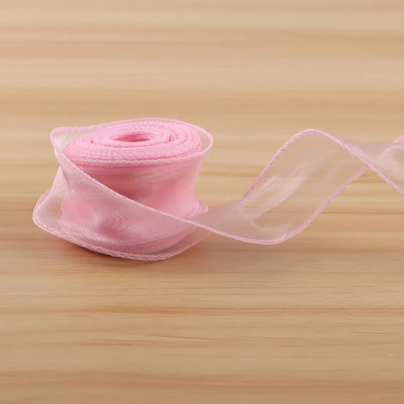 A roll of pink satin ribbon is unwinding onto a wooden surface.