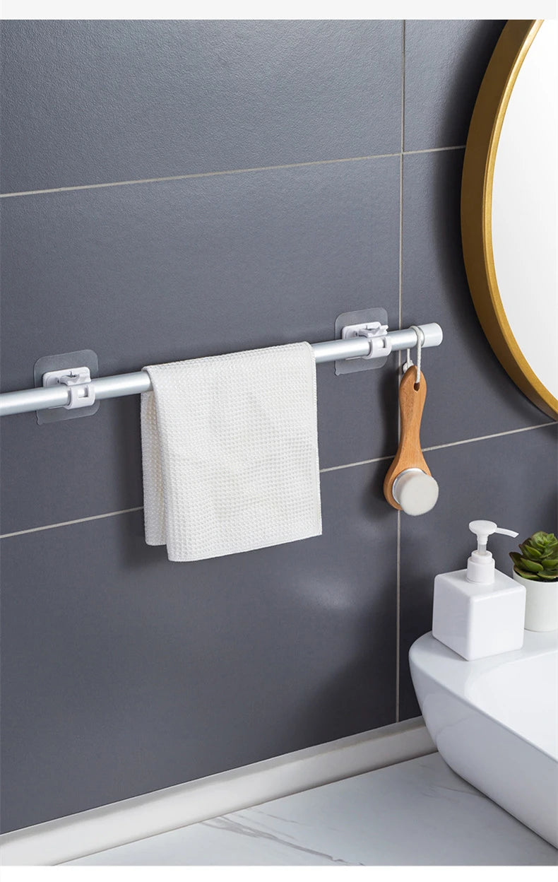 A silver curtain rod with hooks is mounted on a gray wall, holding a white towel and a wooden hanger.