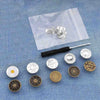 A collection of silver metal button pins is displayed on a translucent plastic sheet against a blue denim background.