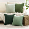 A set of four textured throw pillows in shades of sage green and olive green on a white sofa.