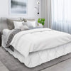 A white duvet and pillows on a bed with a gray headboard and sheer curtains.