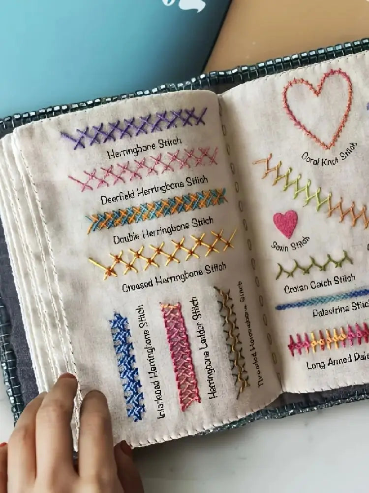 A close-up of a beginner embroidery stitch book showing various herringbone and other decorative stitches on cream fabric.