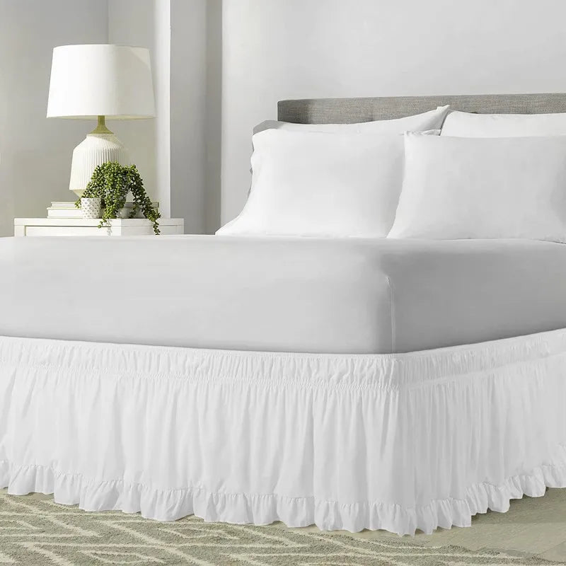 White ruffled bed skirt covering a queen or king bed with white linens and a gray headboard.