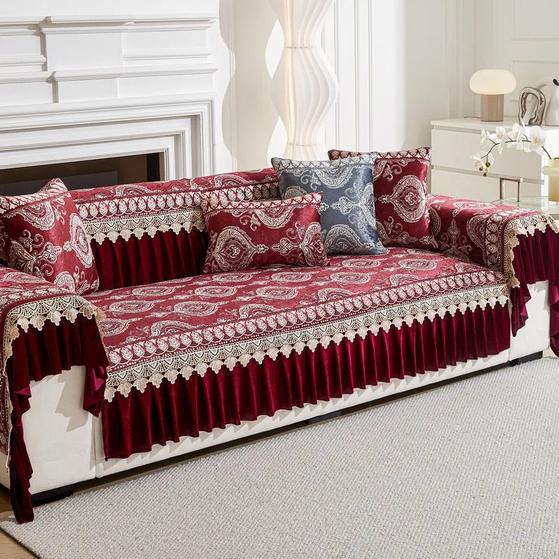A richly patterned red and maroon quilted sofa cover with decorative trim and accent pillows on a white sofa.