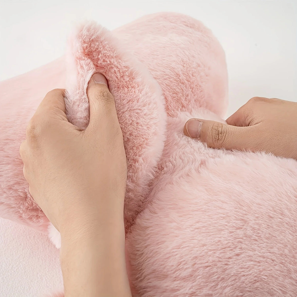 Hands gently touch a fluffy pink decorative bow pillow made of faux fur.