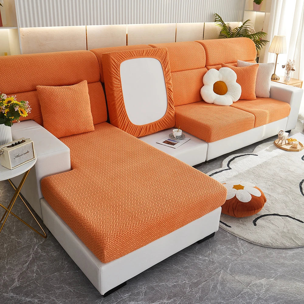 An orange jacquard elastic sofa slipcover with white accents and pillows on a modern living room floor.