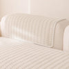 A cream-colored sofa cover with a textured, quilted fabric and a matching fitted throw draped over the back.