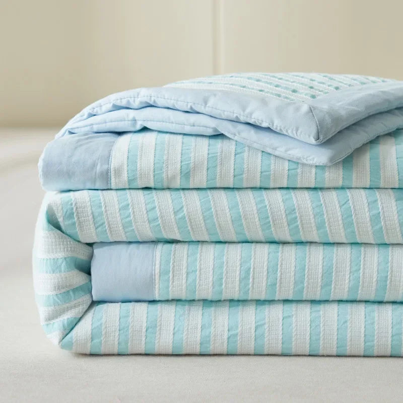 A stack of light blue and white striped luxury jacquard summer quilts.