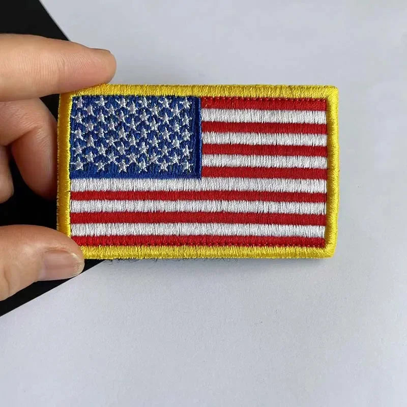 A rectangular patch of the American flag featuring stars and stripes with yellow stitching and hook and loop backing.