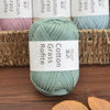 A skein of light green cotton grass yarn resting on a wooden surface next to a woven basket.