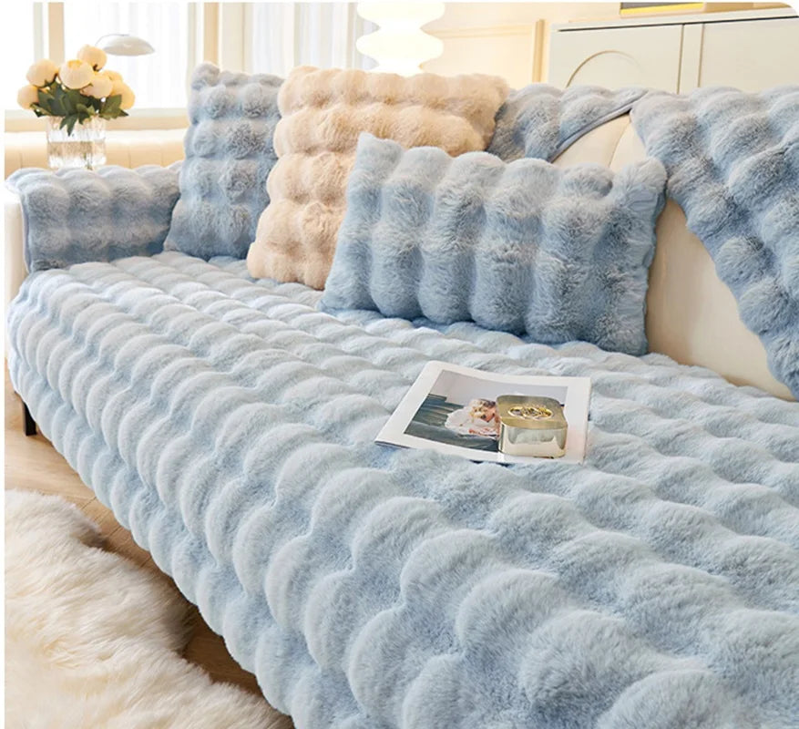 Light blue plush velvet sofa cover with fluffy accent pillows and a white fluffy rug.