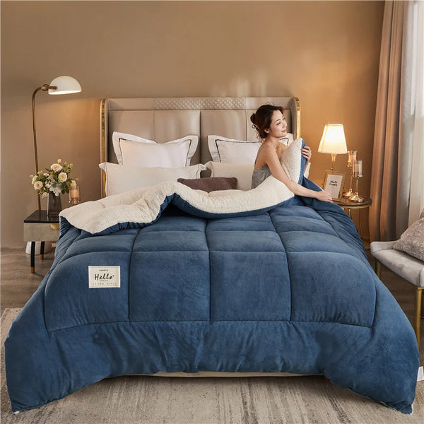 A deep blue weighted fleece blanket is displayed on a bed with light gray bedding and warm lighting.