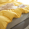 Yellow duvet cover set with pom-pom decoration displayed on a bed.