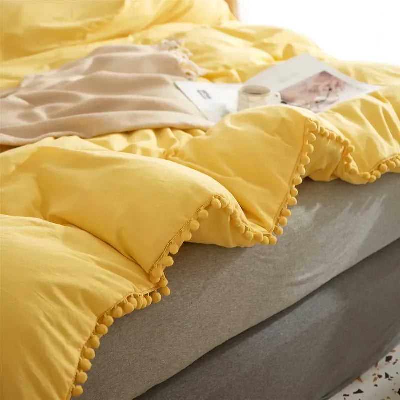 Yellow duvet cover set with pom-pom decoration displayed on a bed.