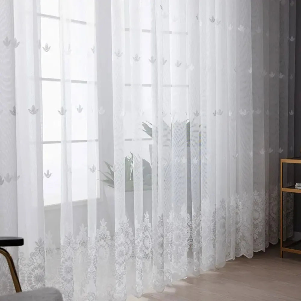 White embroidered floral tulle window curtain hanging in a window frame