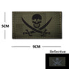 A dark olive green embroidery patch featuring a black skull and crossed swords design on a fabric background.