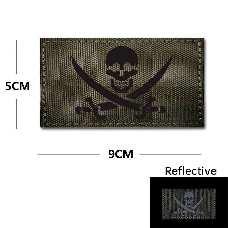 A dark olive green embroidery patch featuring a black skull and crossed swords design on a fabric background.