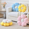 A collection of plush daisy flower throw pillows in blue, yellow, and pink resting on a white sofa.