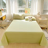 A light green organic cotton flat sheet and pillow set displayed on a bed with white curtains and natural light.