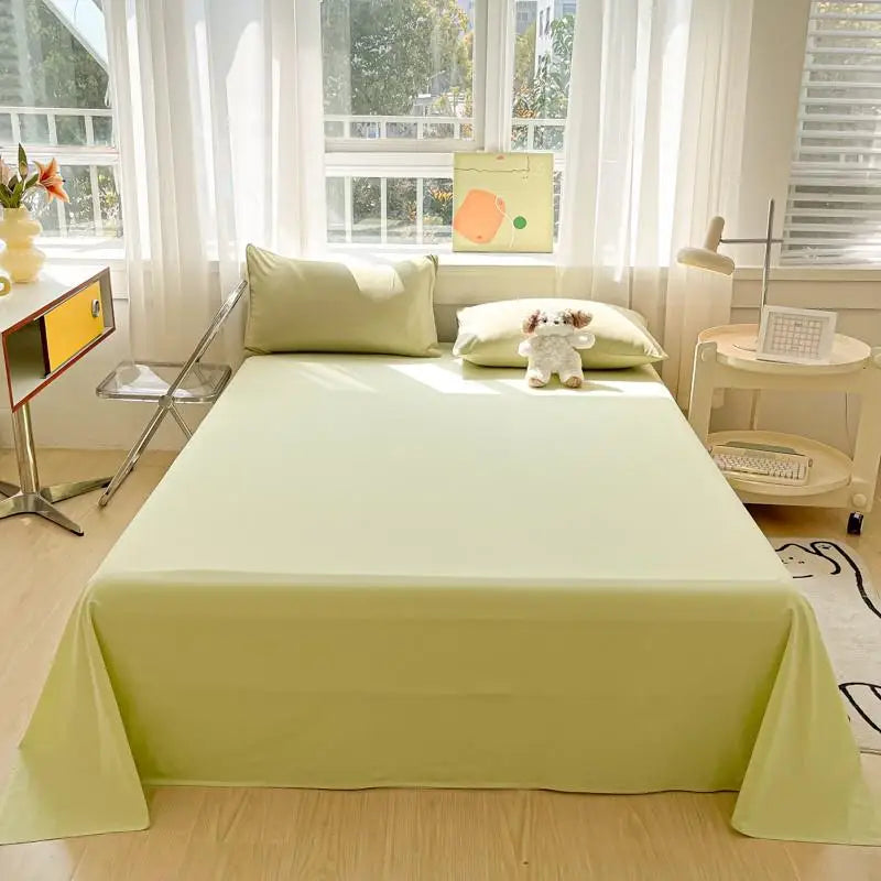A light green organic cotton flat sheet and pillow set displayed on a bed with white curtains and natural light.