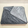 A gray flannel blanket with a light gray reversible side is displayed on a white tiled floor.
