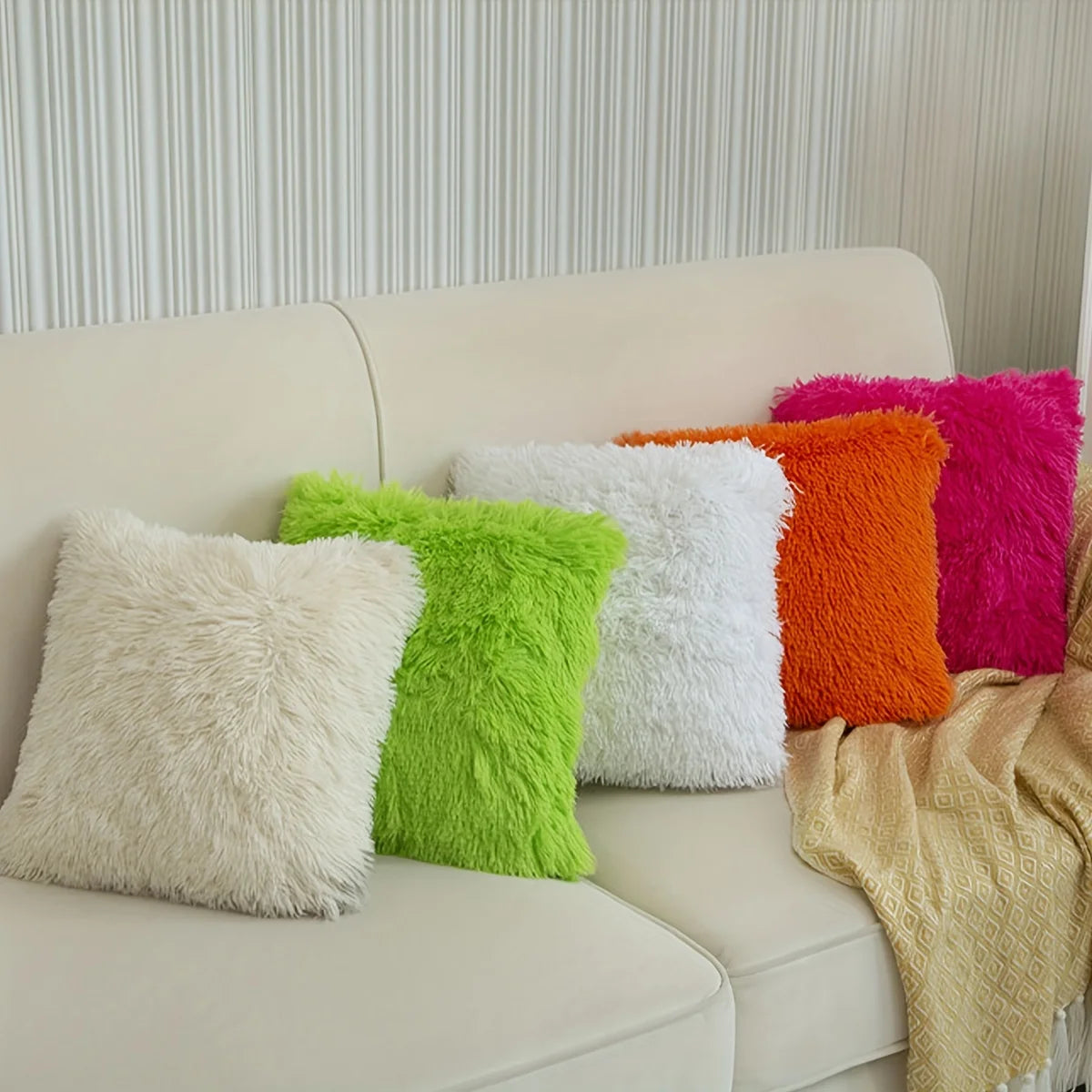 A set of two faux fur throw pillow covers in shades of white, lime green, and orange-yellow displayed on a light sofa.