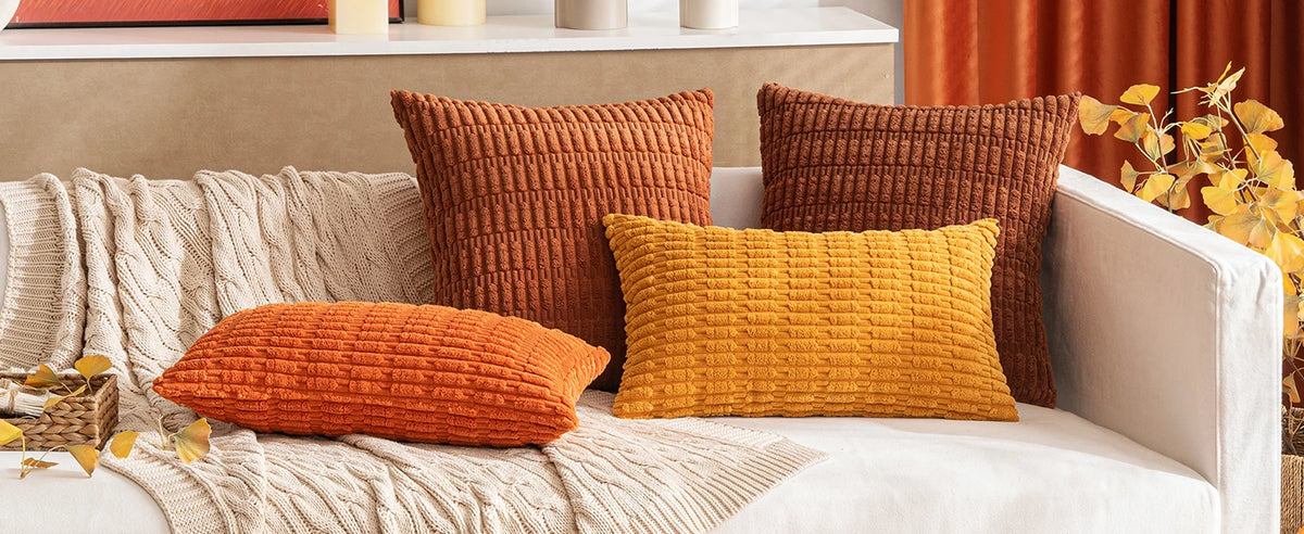 A collection of textured corduroy throw pillows in shades of burnt orange, mustard yellow, and deep brown on a light sofa.