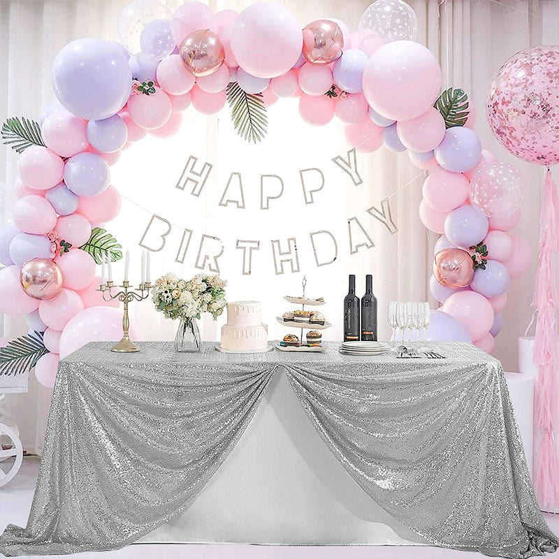 A silver sequin glitter tablecloth draped over a table for a birthday party setup decorated with pink and purple balloons.