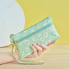 A hand holds a light green PU leather coin purse with a zipper and gold accents against a yellow background.