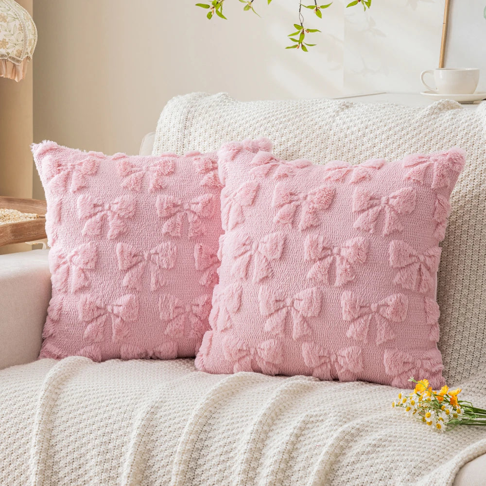 Two pink faux fur pillow covers resting on a cream knitted blanket.
