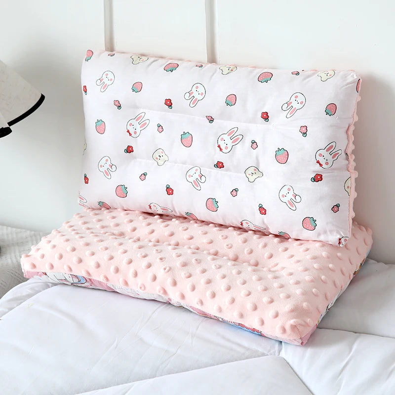 A pink reversible cartoon animal fiber pillow with strawberry and bunny designs resting on white bedding.