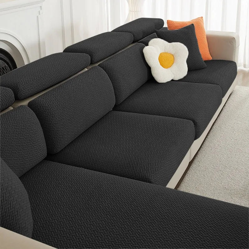 A dark gray jacquard elastic sofa cushion slipcover with decorative orange and white accent pillows.