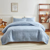 A light blue quilted cotton bedspread set featuring a textured pattern on a bed in a bright room.