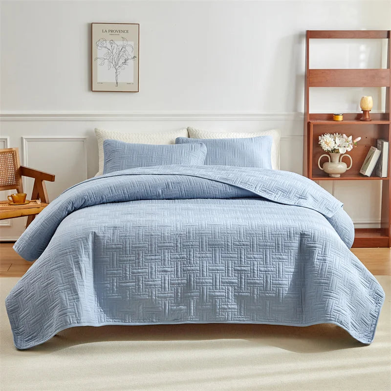 A light blue quilted cotton bedspread set featuring a textured pattern on a bed in a bright room.