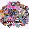 A collection of colorful embroidered letter patches featuring words like LOVE, XOXO, and HOWDY on a gray fabric background.