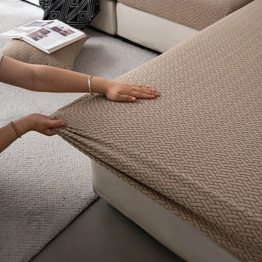 A hand rests on a beige stretchy polar fleece sofa cover, showing the textured fabric and soft upholstery.