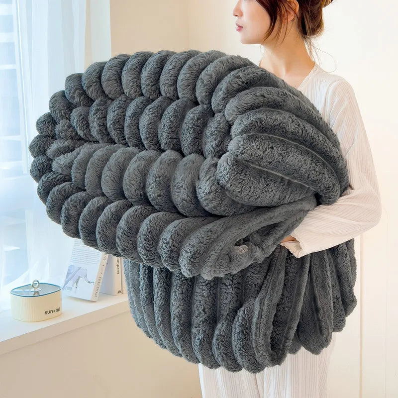 A woman holds a thick, gray, fluffy blanket with vertical stripes against a bright window background.