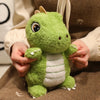 A hand is holding a cute green dinosaur plush toy with white stripes against a brown fabric background.