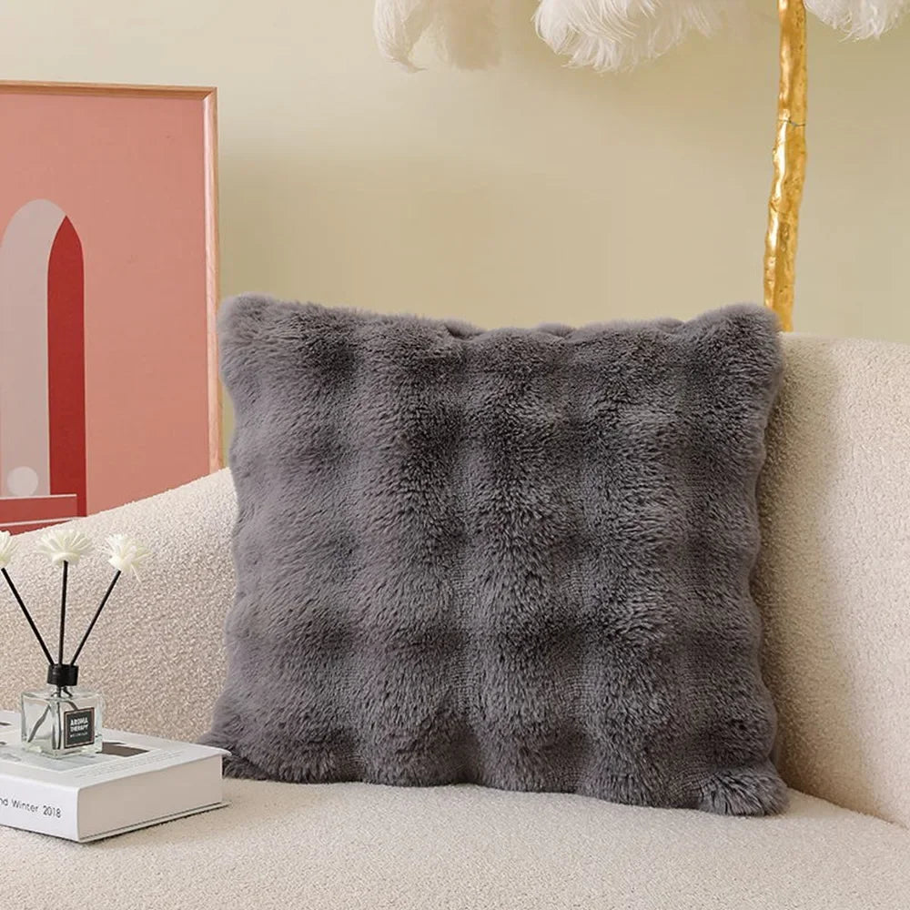 A gray faux fur cushion cover resting on a light-colored sofa.