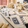 A beige and gray patterned fleece sofa slipcover with fur pillows and a teacup on the cushion.