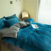 A teal duvet cover set with gray accents is displayed on a bed in a bright room.