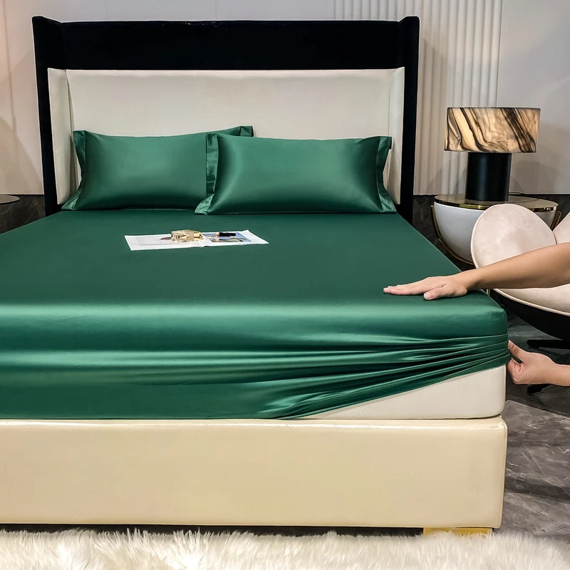 A luxury bed featuring a dark frame, emerald green fitted sheet, and matching pillows on a light-colored mattress.