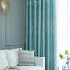 Light blue curtains featuring a white tree pattern hang beside a gray wall and a white sofa.