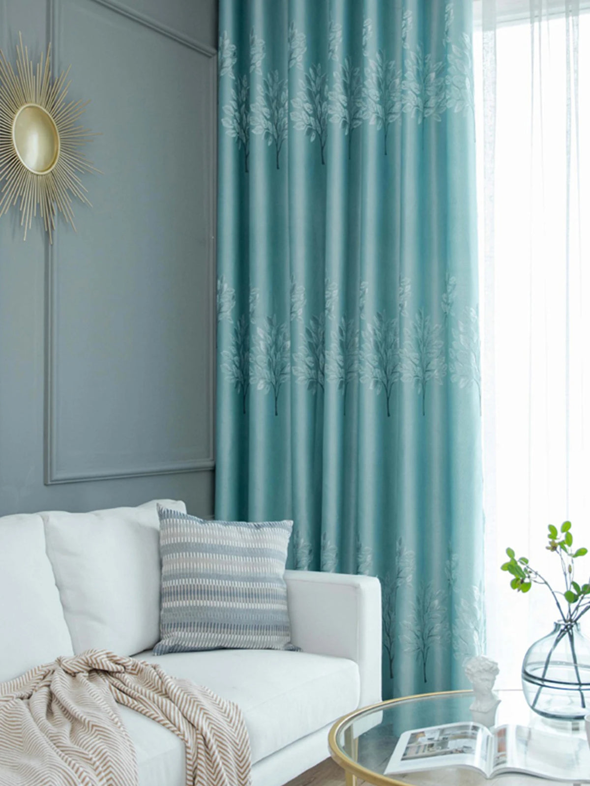 Light blue curtains featuring a white tree pattern hang beside a gray wall and a white sofa.