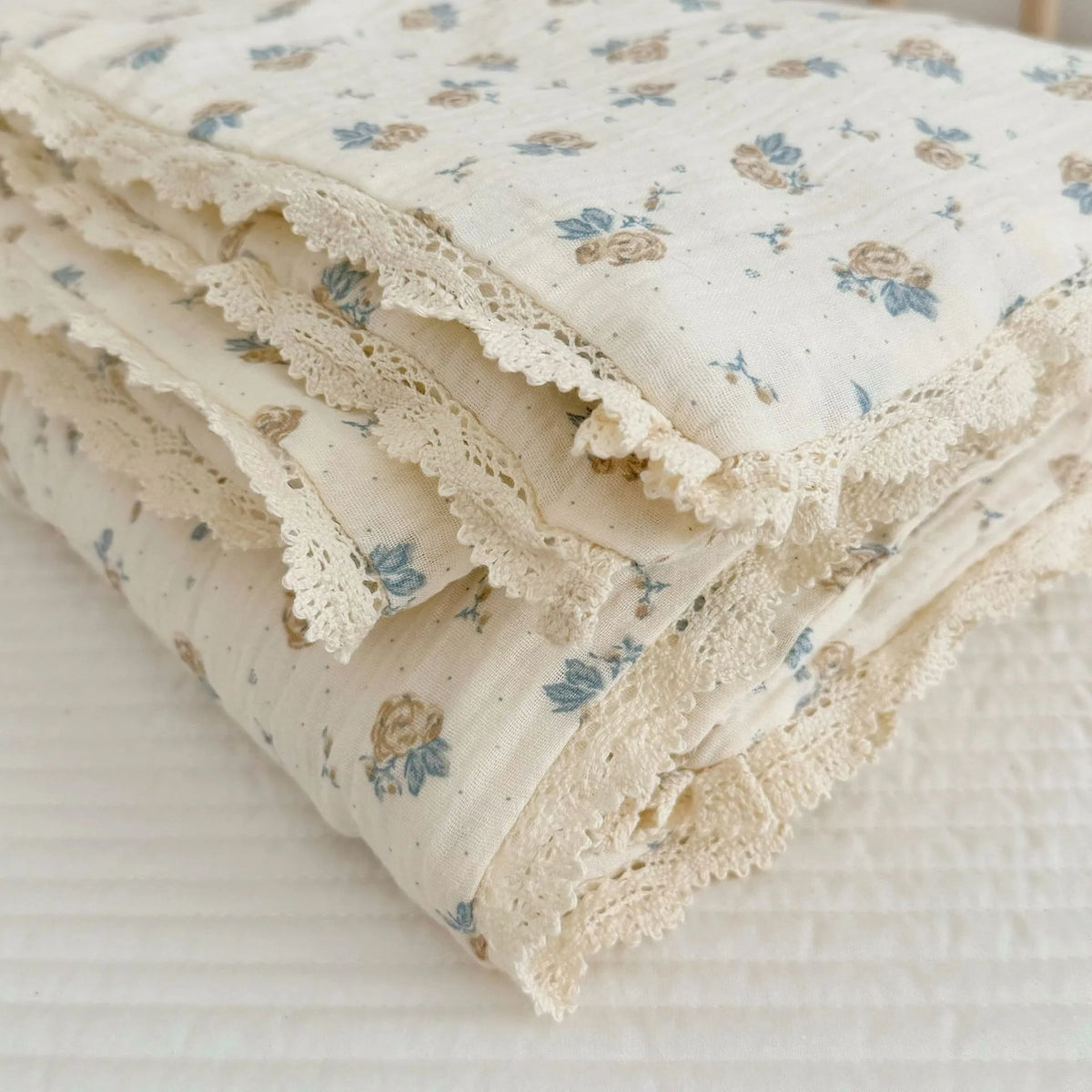 A stack of cream-colored muslin blankets with a blue floral print and delicate lace edges.