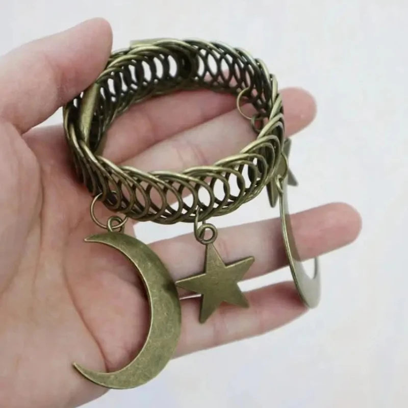 A hand holds a vintage brass curtain clip featuring an intertwined pattern with a crescent moon and a star.