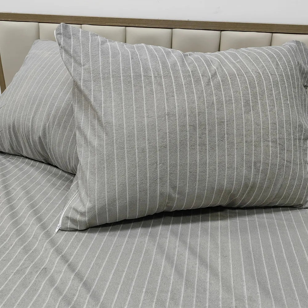 A gray striped pillow protector cover placed on a bed with a headboard.
