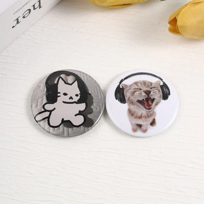 A set of tinplate pins featuring a cat and a kitten with headphones, themed for music and animals.