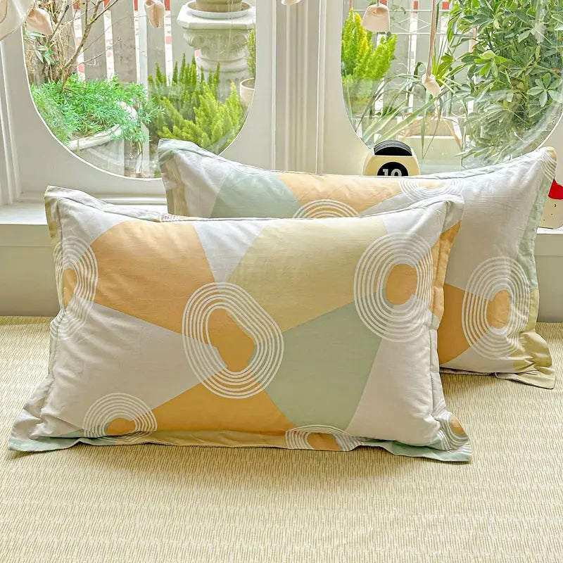 A set of beige and pale green patterned cotton pillows displayed in front of a window with greenery.