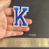 A hand holds a blue and white embroidered letter K patch, measuring 5 by 3.8 centimeters.